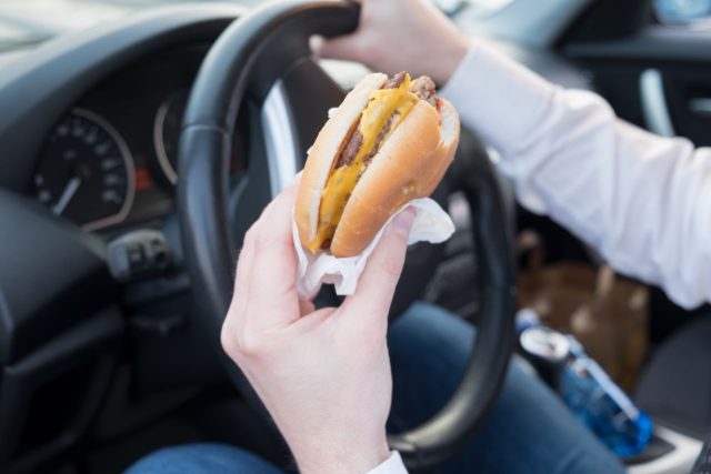 Person eating at the wheel whilst driving which could be a distraction